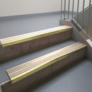 Satin Gold aluminium stair nosing fitted along two concrete steps in an office stairwell, with twin Sahara anti-slip inserts running the full width of each step