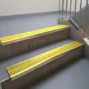 Satin Gold aluminium stair nosing fitted along two concrete steps in an office stairwell, with twin Yellow anti-slip inserts running the full width of each step