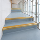 Satin gold aluminium stair nosings with brimstone inserts running the full width of blue-grey vinyl treads in a leisure centre stairwell