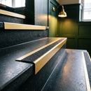 Satin gold aluminium stair nosing with coal insert on dark stone treads in a hotel lobby staircase