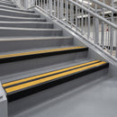 Satin black double channel stair nosings with twin brimstone anti-slip inserts on a railway station staircase