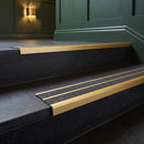 Satin gold double channel stair nosings with twin coal anti-slip inserts on dark stone hotel lobby stair treads