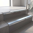 Mirroflect Silver mirror-finish aluminium stair nosing fitted along two concrete steps in an office stairwell, with an Aura anti-slip insert running the full width of each step
