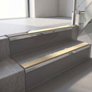 Mirroflect Silver mirror-finish aluminium stair nosing fitted along two concrete steps in an office stairwell, with a Beige anti-slip insert running the full width of each step