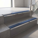 Mirroflect Silver mirror-finish aluminium stair nosing fitted along two concrete steps in an office stairwell, with a Blue anti-slip insert running the full width of each step