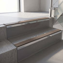 Mirroflect Silver mirror-finish aluminium stair nosing fitted along two concrete steps in an office stairwell, with a Brown anti-slip insert running the full width of each step