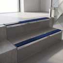Mirroflect Silver mirror-finish aluminium stair nosing fitted along two concrete steps in an office stairwell, with a Dark Blue anti-slip insert running the full width of each step