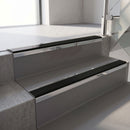 Mirroflect Silver mirror-finish aluminium stair nosing fitted along two concrete steps in an office stairwell, with a Premium Black anti-slip insert running the full width of each step