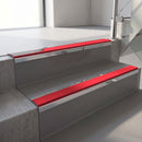 Mirroflect Silver mirror-finish aluminium stair nosing fitted along two concrete steps in an office stairwell, with a Red anti-slip insert running the full width of each step