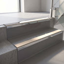 Mirroflect Silver mirror-finish aluminium stair nosing fitted along two concrete steps in an office stairwell, with a Sahara anti-slip insert running the full width of each step