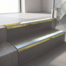 Mirrorflect Gold mirror-finish aluminium stair nosing fitted along two concrete steps in an office stairwell, with an Aura anti-slip insert running the full width of each step