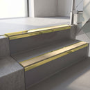 Mirrorflect Gold mirror-finish aluminium stair nosing fitted along two concrete steps in an office stairwell, with a Beige anti-slip insert running the full width of each step