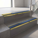 Mirrorflect Gold mirror-finish aluminium stair nosing fitted along two concrete steps in an office stairwell, with a Blue anti-slip insert running the full width of each step