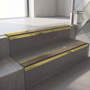 Mirrorflect Gold mirror-finish aluminium stair nosing fitted along two concrete steps in an office stairwell, with a Brown anti-slip insert running the full width of each step