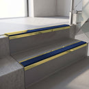 Mirrorflect Gold mirror-finish aluminium stair nosing fitted along two concrete steps in an office stairwell, with a Dark Blue anti-slip insert running the full width of each step