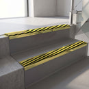 Mirrorflect Gold mirror-finish aluminium stair nosing fitted along two concrete steps in an office stairwell, with a black and yellow Hazard anti-slip insert running the full width of each step