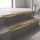 Mirrorflect Gold mirror-finish aluminium stair nosing fitted along two concrete steps in an office stairwell, with a Mid Brown anti-slip insert running the full width of each step