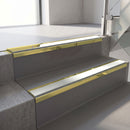 Mirrorflect Gold mirror-finish aluminium stair nosing fitted along two concrete steps in an office stairwell, with an Oyster anti-slip insert running the full width of each step