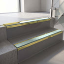 Mirrorflect Gold mirror-finish aluminium stair nosing fitted along two concrete steps in an office stairwell, with a Sage Green anti-slip insert running the full width of each step