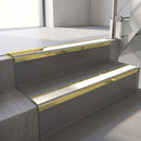 Mirrorflect Gold mirror-finish aluminium stair nosing fitted along two concrete steps in an office stairwell, with a White anti-slip insert running the full width of each step