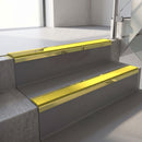 Mirrorflect Gold mirror-finish aluminium stair nosing fitted along two concrete steps in an office stairwell, with a Yellow anti-slip insert running the full width of each step