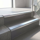 Square-edge aluminium stair nosing fitted along two concrete steps in an office stairwell, with an Aura anti-slip insert running the full width of each step
