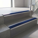 Square-edge aluminium stair nosing fitted along two concrete steps in an office stairwell, with a Dark Blue anti-slip insert running the full width of each step