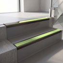 Dark Bronze aluminium stair nosing fitted along two concrete steps in an office stairwell, with an Apple Green anti-slip insert running the full width of each step