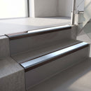 Dark Bronze aluminium stair nosing fitted along two concrete steps in an office stairwell, with an Aura anti-slip insert running the full width of each step