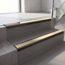 Dark Bronze aluminium stair nosing fitted along two concrete steps in an office stairwell, with a Beige anti-slip insert running the full width of each step