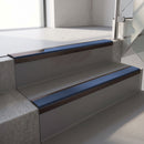 Dark Bronze aluminium stair nosing fitted along two concrete steps in an office stairwell, with a Blue anti-slip insert running the full width of each step