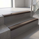 Dark Bronze aluminium stair nosing fitted along two concrete steps in an office stairwell, with a Brown anti-slip insert running the full width of each step