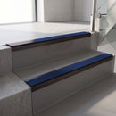 Dark Bronze aluminium stair nosing fitted along two concrete steps in an office stairwell, with a Dark Blue anti-slip insert running the full width of each step