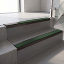 Dark Bronze aluminium stair nosing fitted along two concrete steps in an office stairwell, with a Dark Green anti-slip insert running the full width of each step