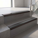 Dark Bronze aluminium stair nosing fitted along two concrete steps in an office stairwell, with a Dark Grey anti-slip insert running the full width of each step