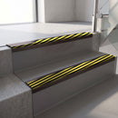 Dark Bronze aluminium stair nosing fitted along two concrete steps in an office stairwell, with a black and yellow Hazard anti-slip insert running the full width of each step