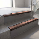 Dark Bronze aluminium stair nosing fitted along two concrete steps in an office stairwell, with a Mid Brown anti-slip insert running the full width of each step