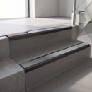 Dark Bronze aluminium stair nosing fitted along two concrete steps in an office stairwell, with a Mid Grey anti-slip insert running the full width of each step