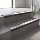 Dark Bronze aluminium stair nosing fitted along two concrete steps in an office stairwell, with a Polar Grey anti-slip insert running the full width of each step