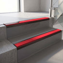 Dark Bronze aluminium stair nosing fitted along two concrete steps in an office stairwell, with a Red anti-slip insert running the full width of each step