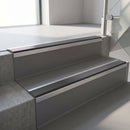 Square-edge aluminium stair nosing fitted along two concrete steps in an office stairwell, with a Dark Grey anti-slip insert running the full width of each step