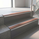 Square-edge aluminium stair nosing fitted along two concrete steps in an office stairwell, with a Mid Brown anti-slip insert running the full width of each step