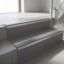 Square-edge aluminium stair nosing fitted along two concrete steps in an office stairwell, with a Mid Grey anti-slip insert running the full width of each step