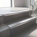 Square-edge aluminium stair nosing fitted along two concrete steps in an office stairwell, with a Polar Grey anti-slip insert running the full width of each step