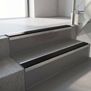 Square-edge aluminium stair nosing fitted along two concrete steps in an office stairwell, with a Premium Black anti-slip insert running the full width of each step