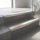 Square-edge aluminium stair nosing fitted along two concrete steps in an office stairwell, with a Sahara anti-slip insert running the full width of each step