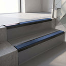 Satin Black aluminium stair nosing fitted along two concrete steps in an office stairwell, with a Blue anti-slip insert running the full width of each step