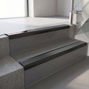 Satin Black aluminium stair nosing fitted along two concrete steps in an office stairwell, with a Dark Grey anti-slip insert running the full width of each step