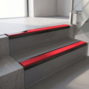Satin Black aluminium stair nosing fitted along two concrete steps in an office stairwell, with a Red anti-slip insert running the full width of each step