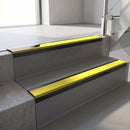 Satin Black aluminium stair nosing fitted along two concrete steps in an office stairwell, with a Yellow anti-slip insert running the full width of each step